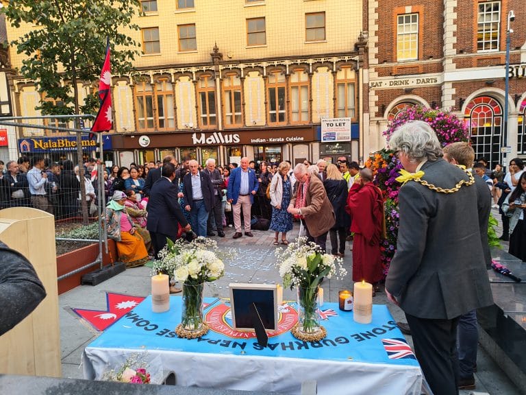 Mourners around a candlelit memorial table draped with a Maidstone Gurkha Nepalese Community banner in Jubilee Square, Maidstone.