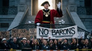 Illustration: a mayor in ceremonial robes and tricorn hat stands on city hall steps with a raised, white-gloved hand, while protesters below hold placards reading 'No Barons', 'End the Dynasty' and 'People over Patrons' — depicting the editorial thesis of Edition B of Kent Local News' Kent LGR Part 3 reader guide.