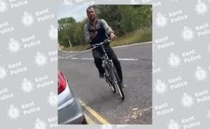 A man riding a bicycle while holding a mobile phone, in an image released by Kent Police