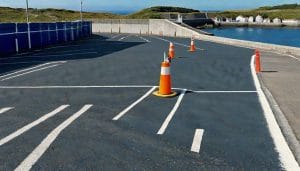 An empty coastal car park with white bay markings and a calm sea visible beyond a low harbour wall