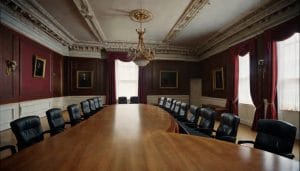 Empty modern British council chamber with curved wooden desks and upholstered chairs under soft overhead lighting